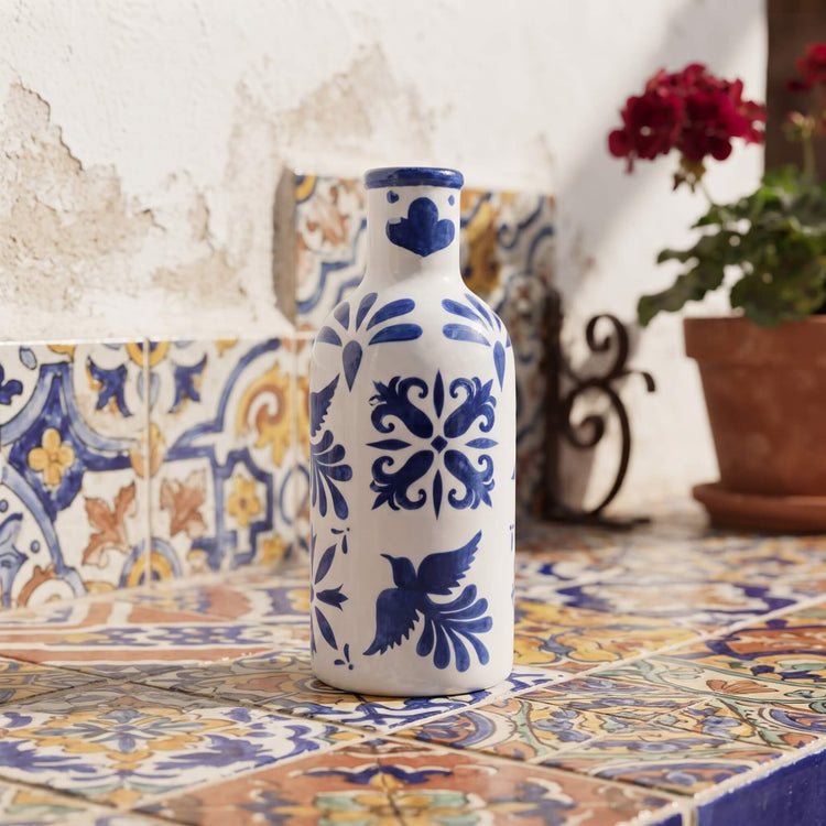 Aceitera de cerámica artesanal Raíces pintada a mano en azul cobalto junto a flores y patio andaluz Kinara.
